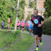 Runner wearing number 2 leads a group of runners along a tree-lined path during a charity running event in Lichfield.