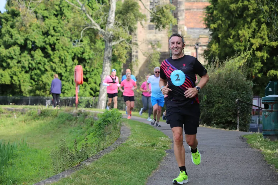 Runner wearing number 2 leads a group of runners along a tree-lined path during a charity running event in Lichfield.